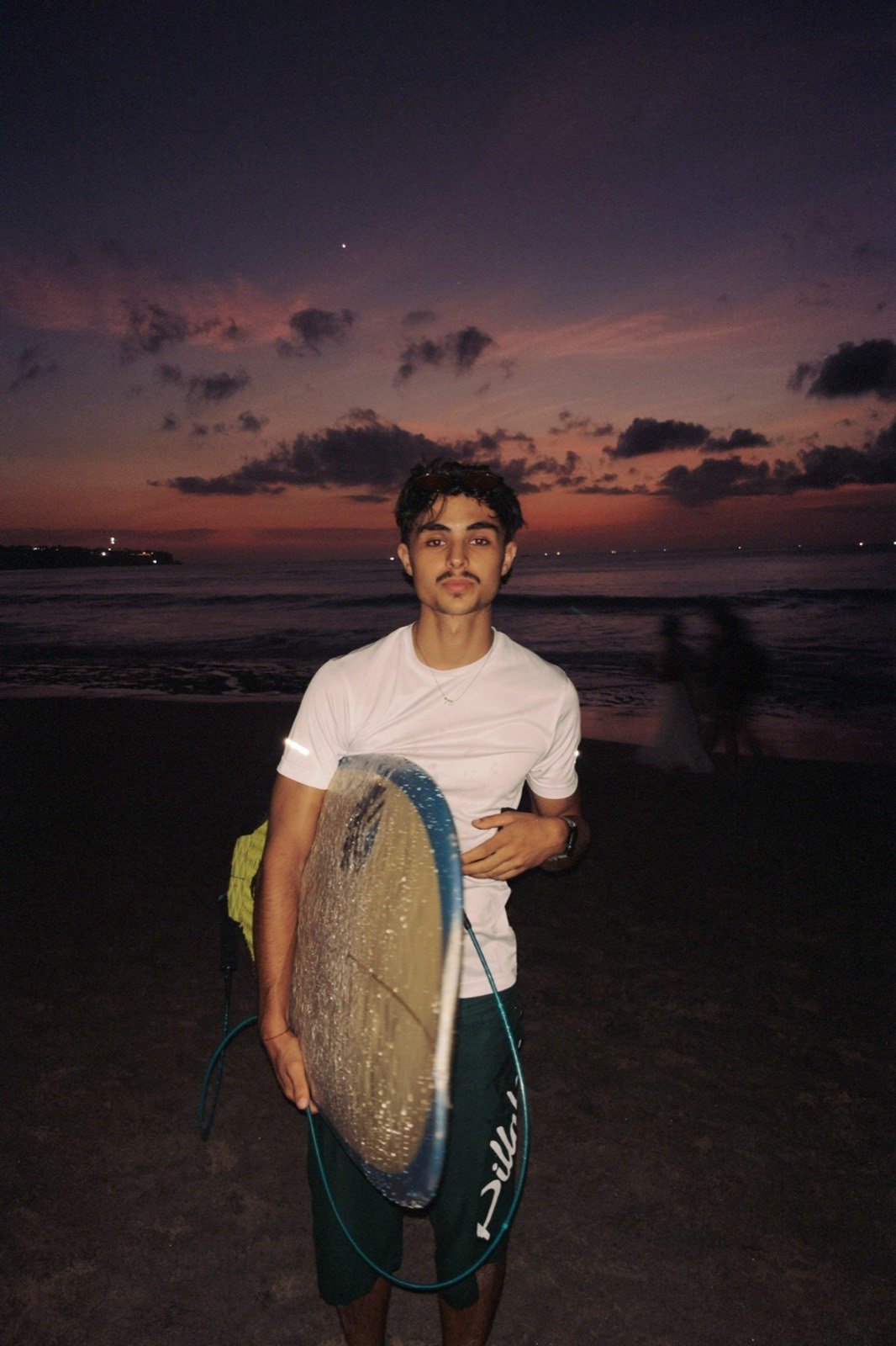 Pablo Gómez con su tabla de surf en la playa al atardecer